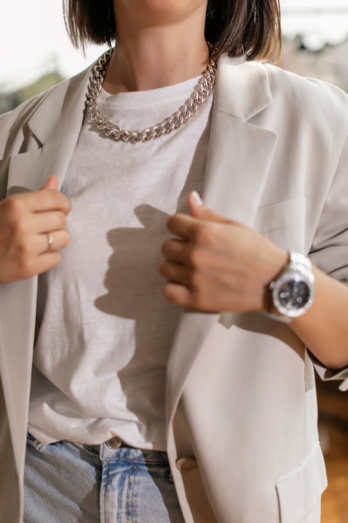 Fashion-forward woman in blazer, white t-shirt, silver necklace, and wristwatch fashionably adjusting her attire.