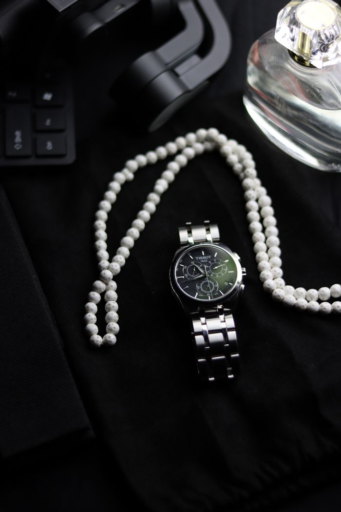 Close-up of a chronograph watch paired with a pearl necklace on a black background.